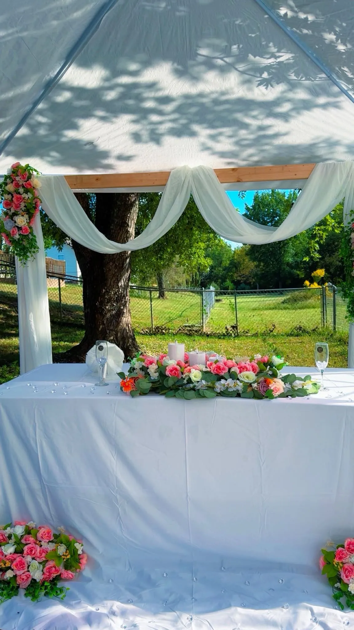 Mesa vestida de blanco con un arreglo de flores bajo una carpa con telas colgadas